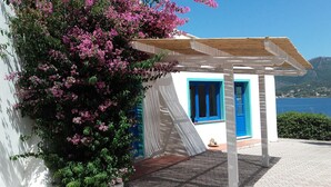 A white building with blue doors and windows, a wooden pergola, and pink flowering bushes. - Hotel Grotte del Paradiso (Portoferraio)