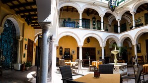 Een ruime binnenplaats met meerdere niveaus, inclusief een centrale fontein, buitenmeubilair en diverse architectonische details zoals bogen en zuilen.