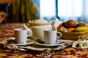 Une table dressée pour le petit-déjeuner avec deux tasses blanches, une théière, une cuillère, un couteau et un panier de fruits, le tout posé sur une nappe à motifs.