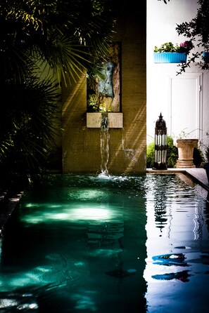 Una piscina interior tranquila con una fuente, rodeada de abundante follaje y detalles arquitectónicos.