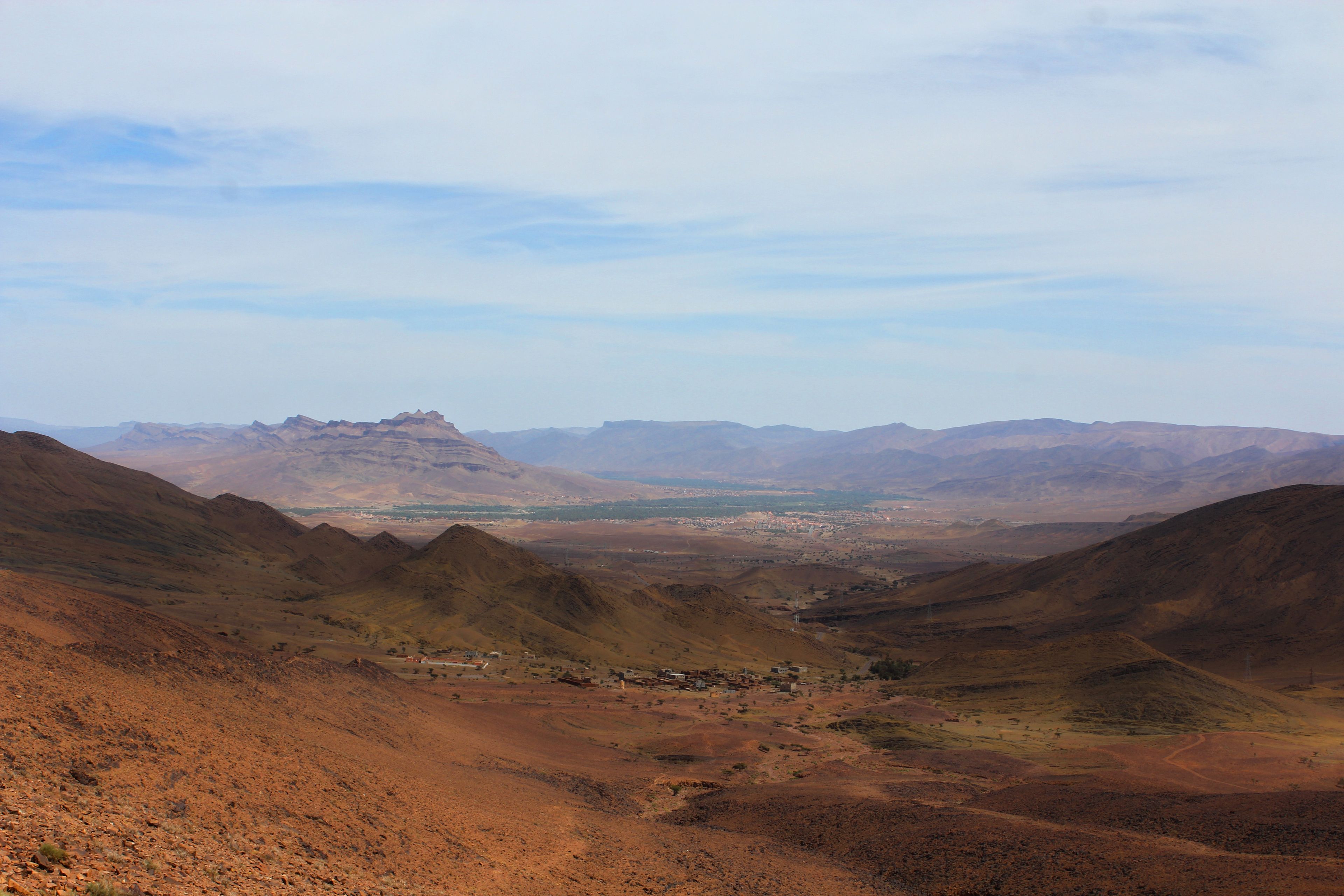 A panoramic view of a mountainous landscape with a valley and distant hills.