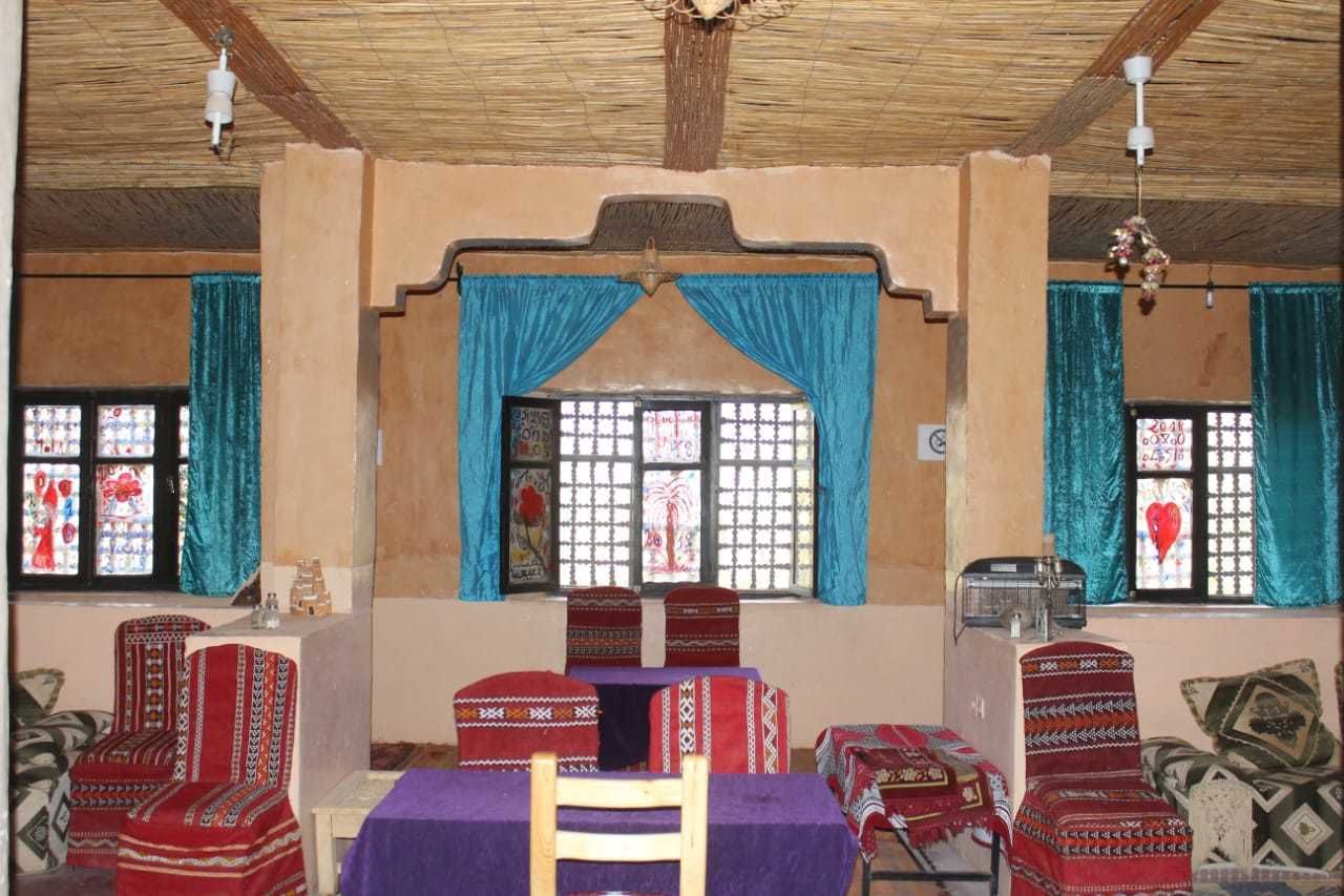 A room with a wooden ceiling, a central window with blue curtains, and patterned furniture.