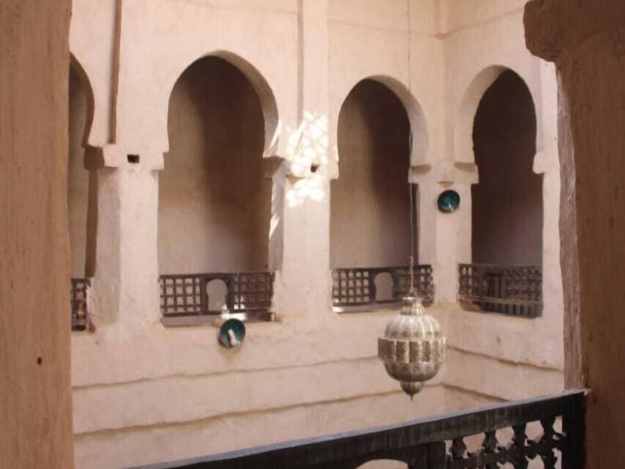 Une cour intérieure agrémentée d’arcades, d’une lanterne suspendue et d’un plafond en bois.
