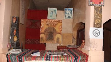Una habitación con alfombra estampada, una cama con manta roja, un teléfono instalado en la pared y cuadros enmarcados.