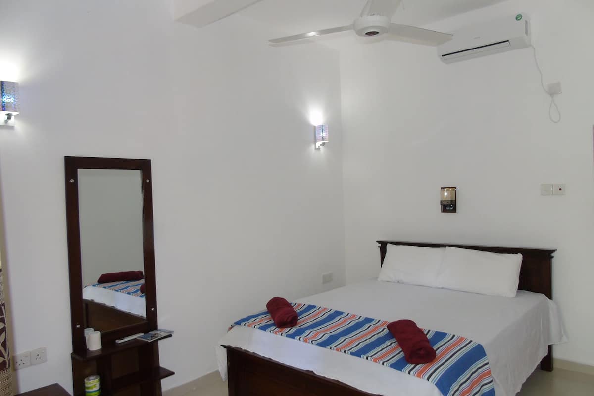 Une chambre d’hôtel équipée d’un lit, d’un ventilateur de plafond, d’un climatiseur, d’un miroir et d’une table de chevet.