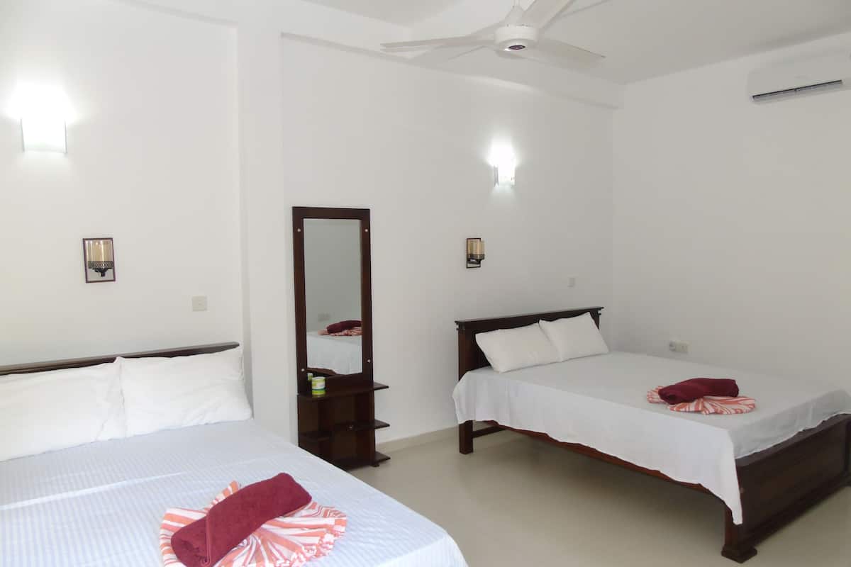 Une chambre d’hôtel avec deux lits simples, un ventilateur de plafond et un grand miroir.