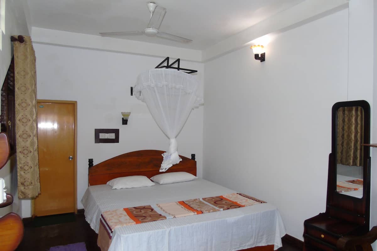 Une chambre à coucher avec un lit, un ventilateur de plafond, une table de chevet, un miroir et une porte.