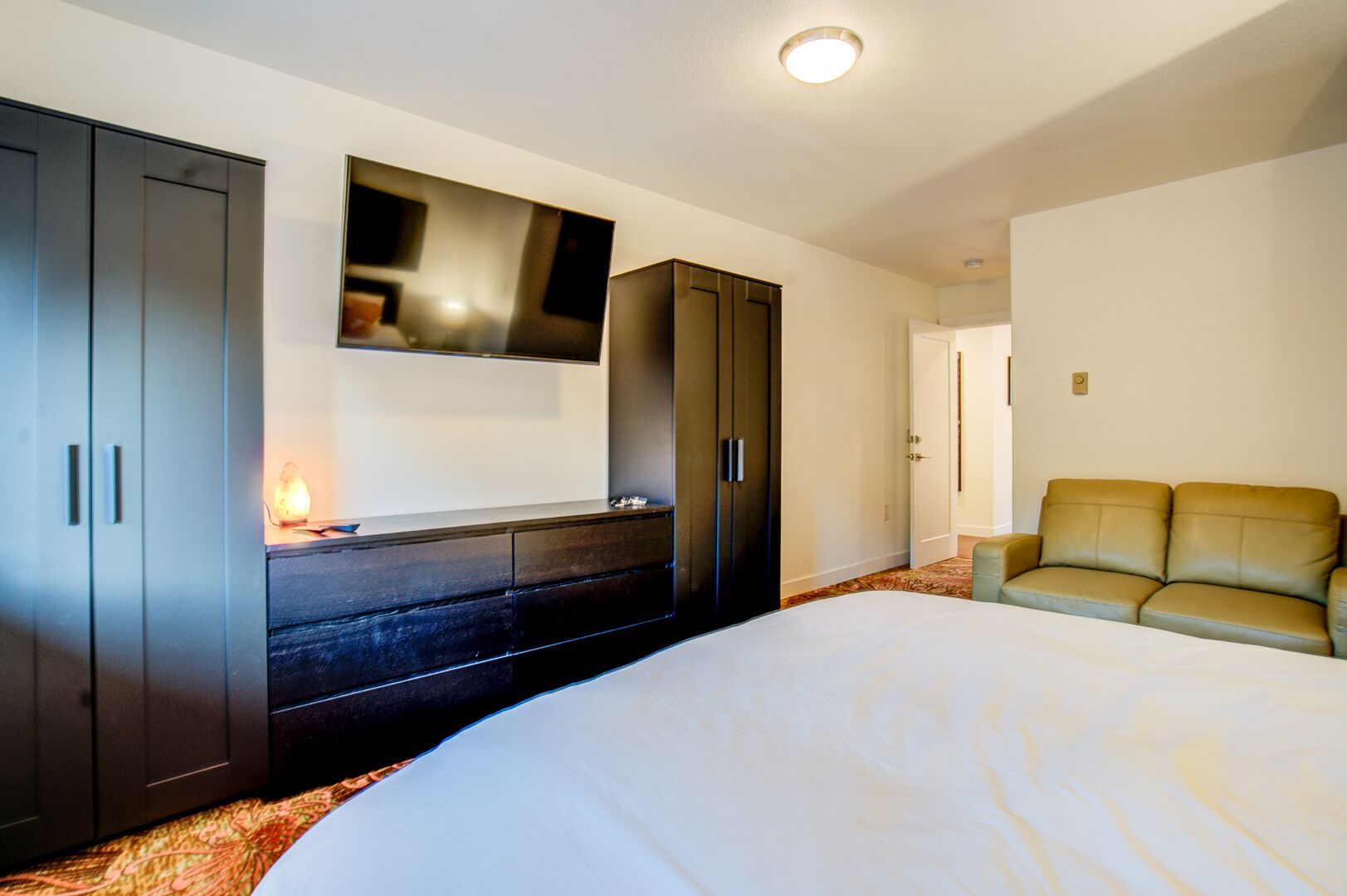 A hotel room with a large bed, a dark wooden dresser, a flat-screen TV mounted above it, and a green leather sofa.