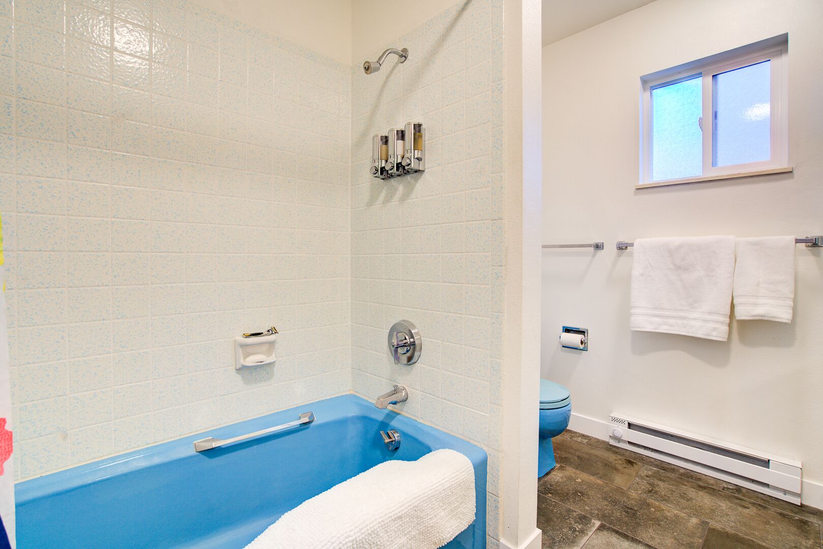 A bathroom with a blue bathtub, white tiles, a shower, and a window.