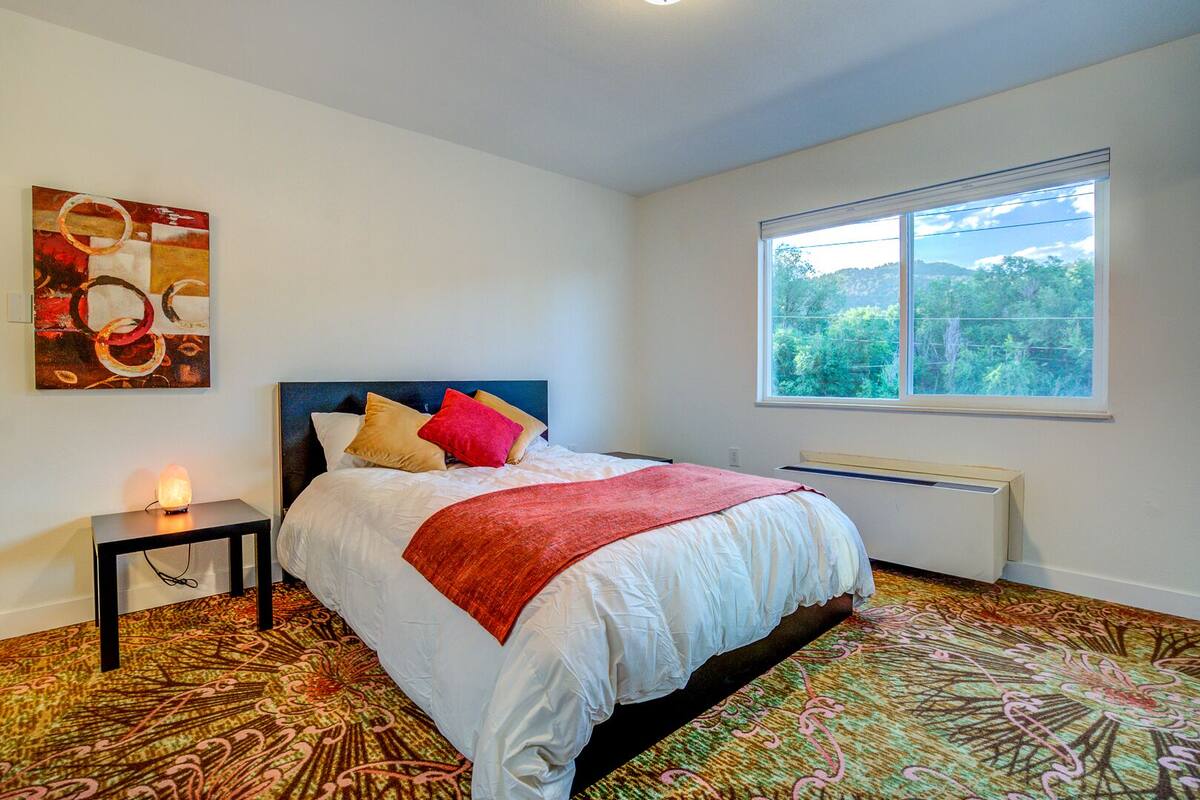 Un dormitorio con cama, mesita de noche, calefactor, ventana y un cuadro en la pared.