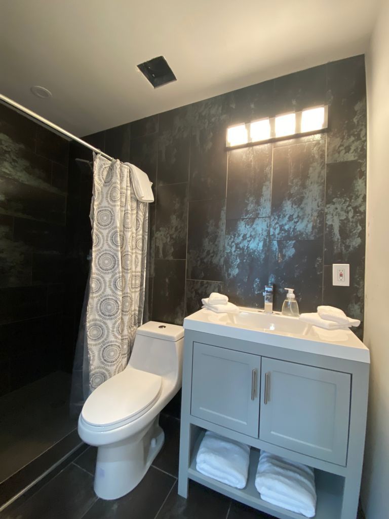 A modern bathroom with a toilet, a shower with a patterned curtain, and a vanity with a mirror and two sinks.
