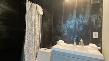 A modern bathroom with a toilet, a shower with a patterned curtain, and a vanity with a mirror and two sinks.