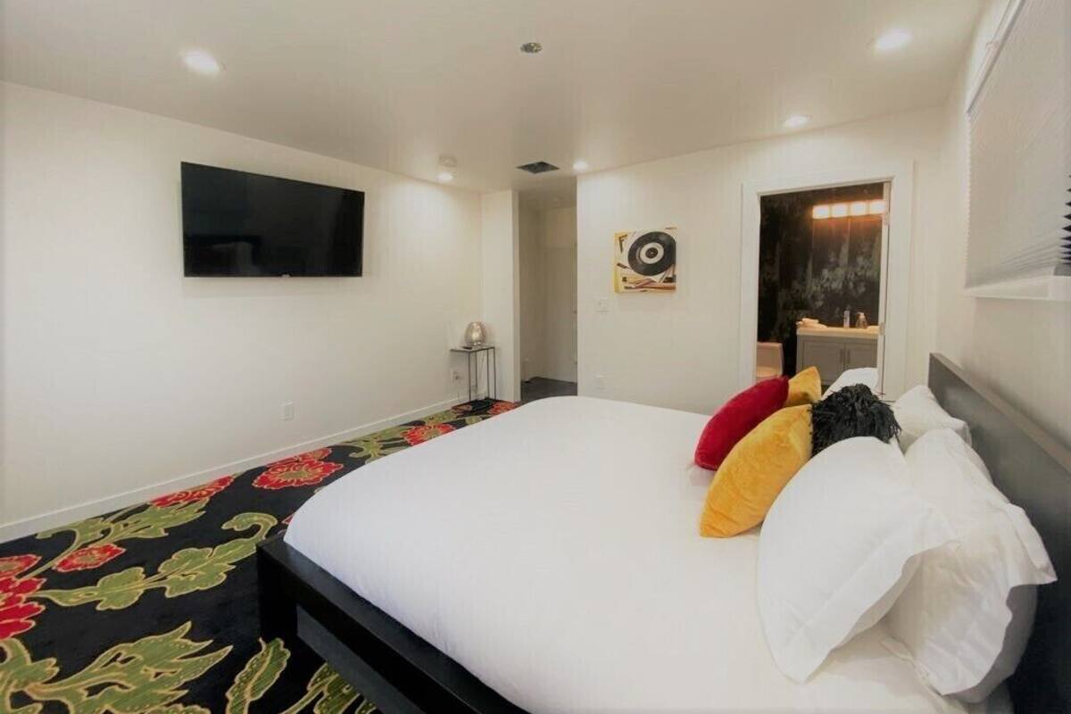 Habitación de hotel con una cama grande, un televisor de pantalla plana montado en la pared, una mesita de noche con lámpara y un adorno decorativo en la pared.