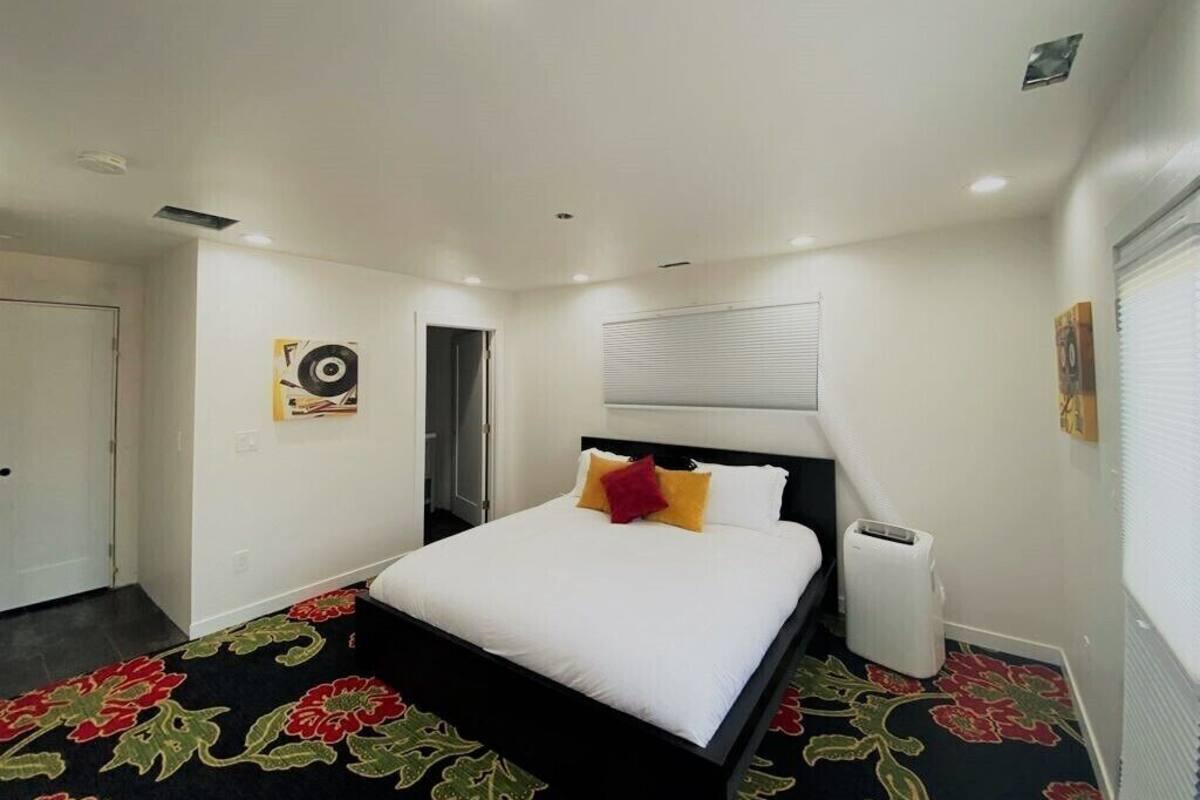 Una habitación de hotel con una cama, un radiador, una puerta y una pared con un cuadro.