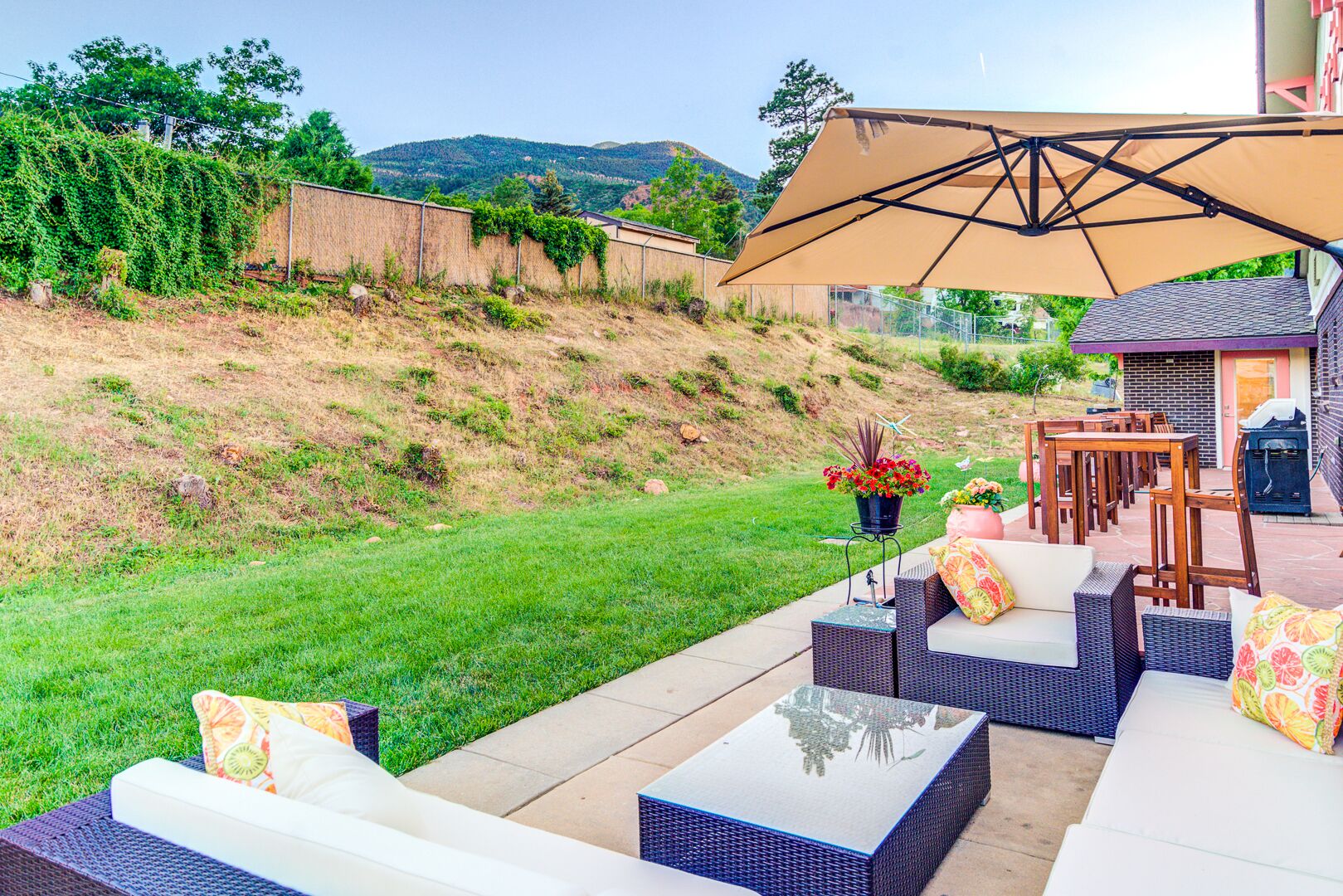 An outdoor patio with wicker furniture, a large umbrella, and a view of a hilly landscape.