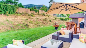 An outdoor patio with wicker furniture, a large umbrella, and a view of a hilly landscape.