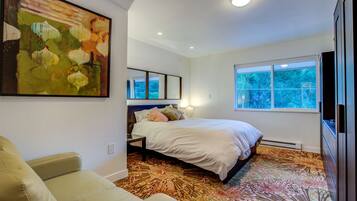 A bedroom with a bed, a sofa, a large painting, a window, and a mirror.