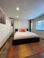 Un dormitorio moderno con una cama grande, una alfombra colorida y una ventana con persianas.