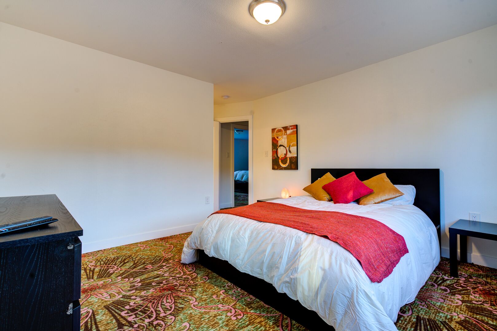 A bedroom with a bed, a bedside table, a nightstand, a carpet, and a ceiling light.
