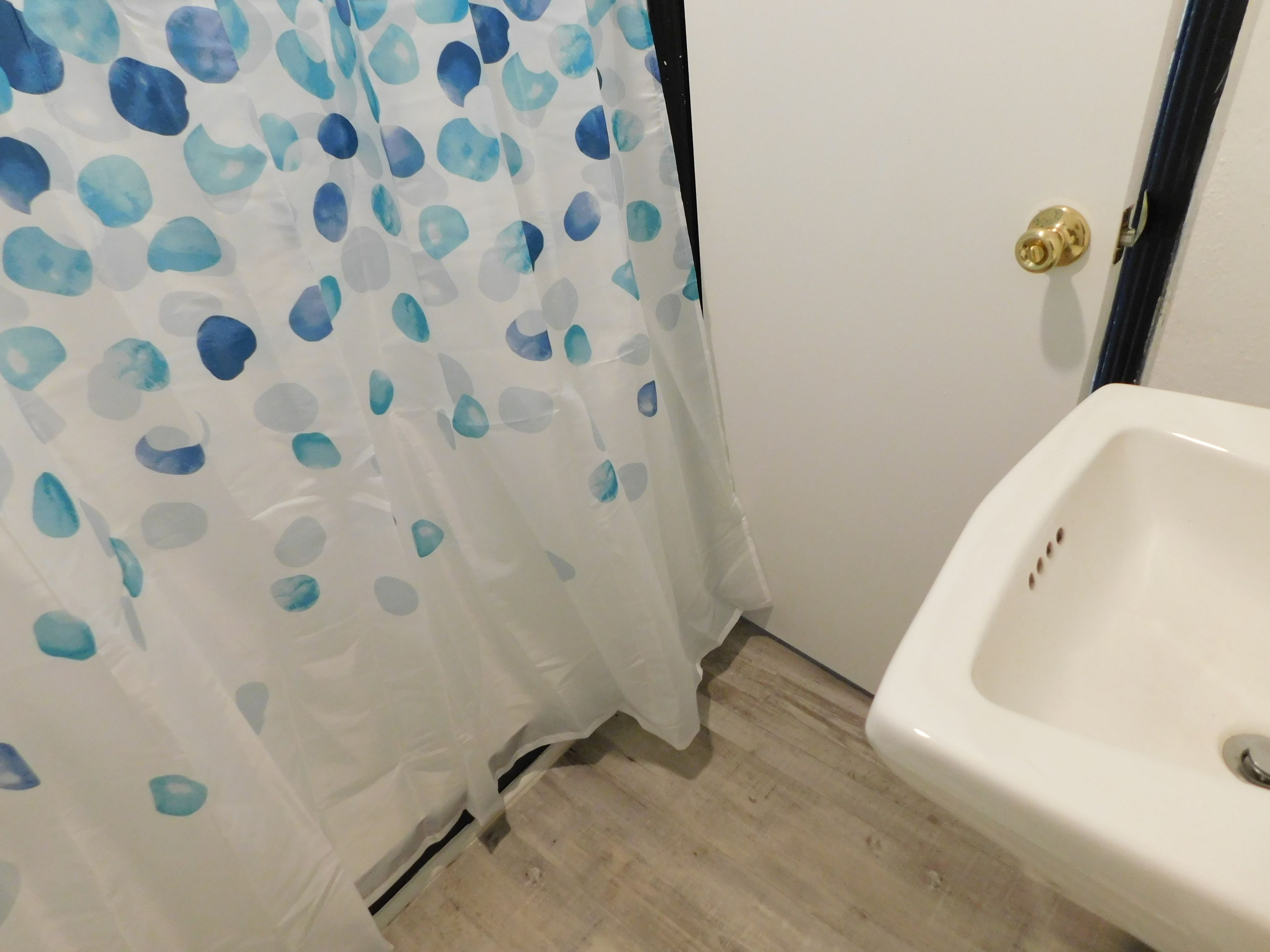 A bathroom with a white sink, a blue and white shower curtain, and a wooden floor.