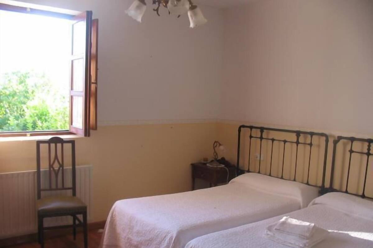 Quarto com duas camas, uma cadeira, uma mesa de cabeceira e uma janela.