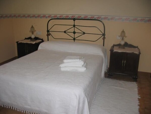 A neatly made bed with white linens and a decorative headboard. There are two bedside tables with lamps. - Casa Pousadoira (Mino)
