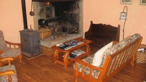 A cozy living room with a fireplace, wooden furniture, and a stone wall. - Casa Pousadoira (Mino)