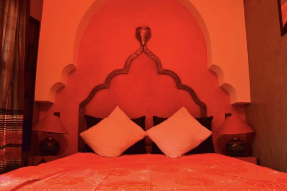 A bed with a red headboard and two matching pillows, a lamp on each side, and a patterned bedspread.