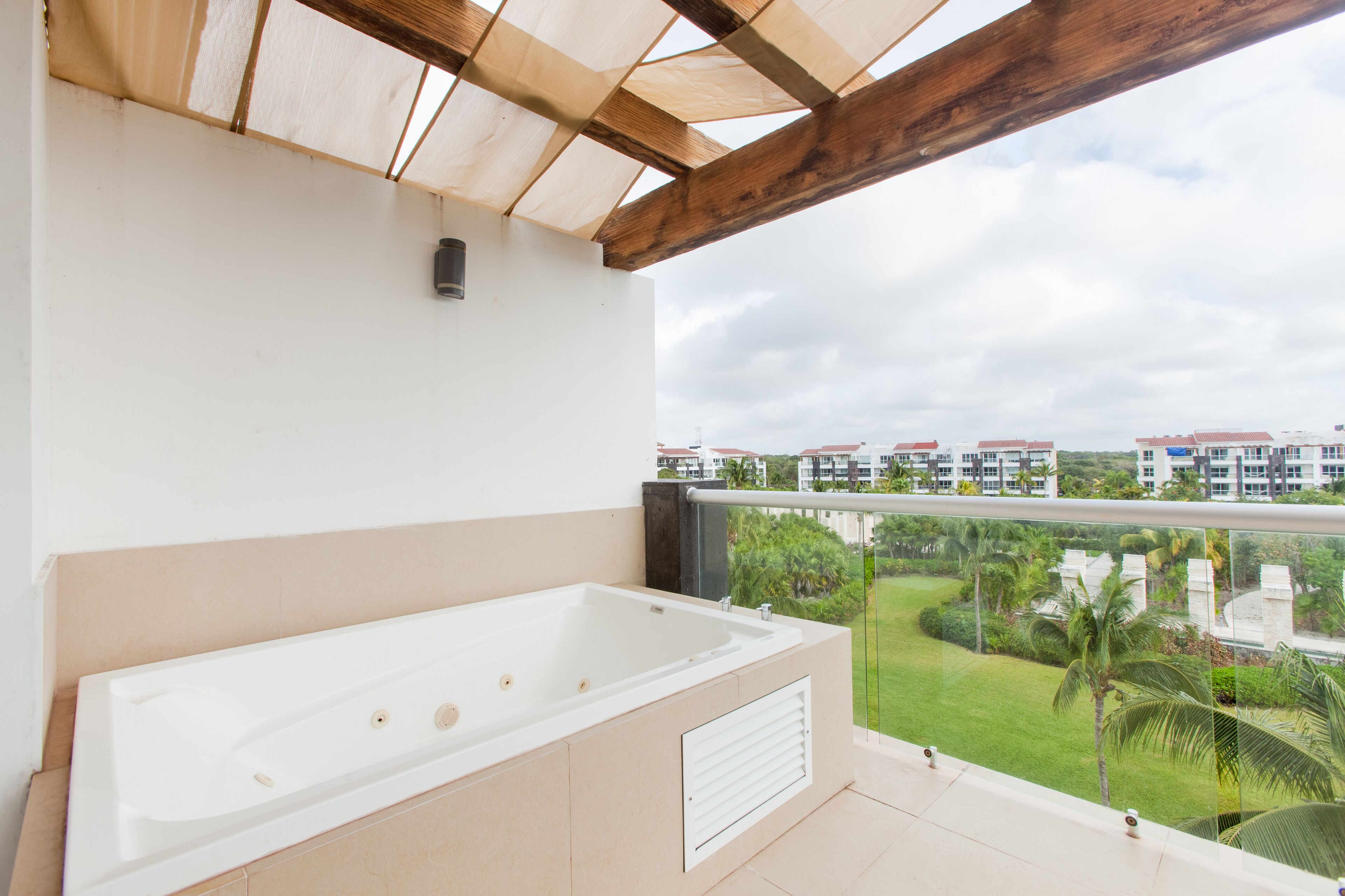 Un balcón con una bañera blanca, techo de madera y vista a una zona residencial.