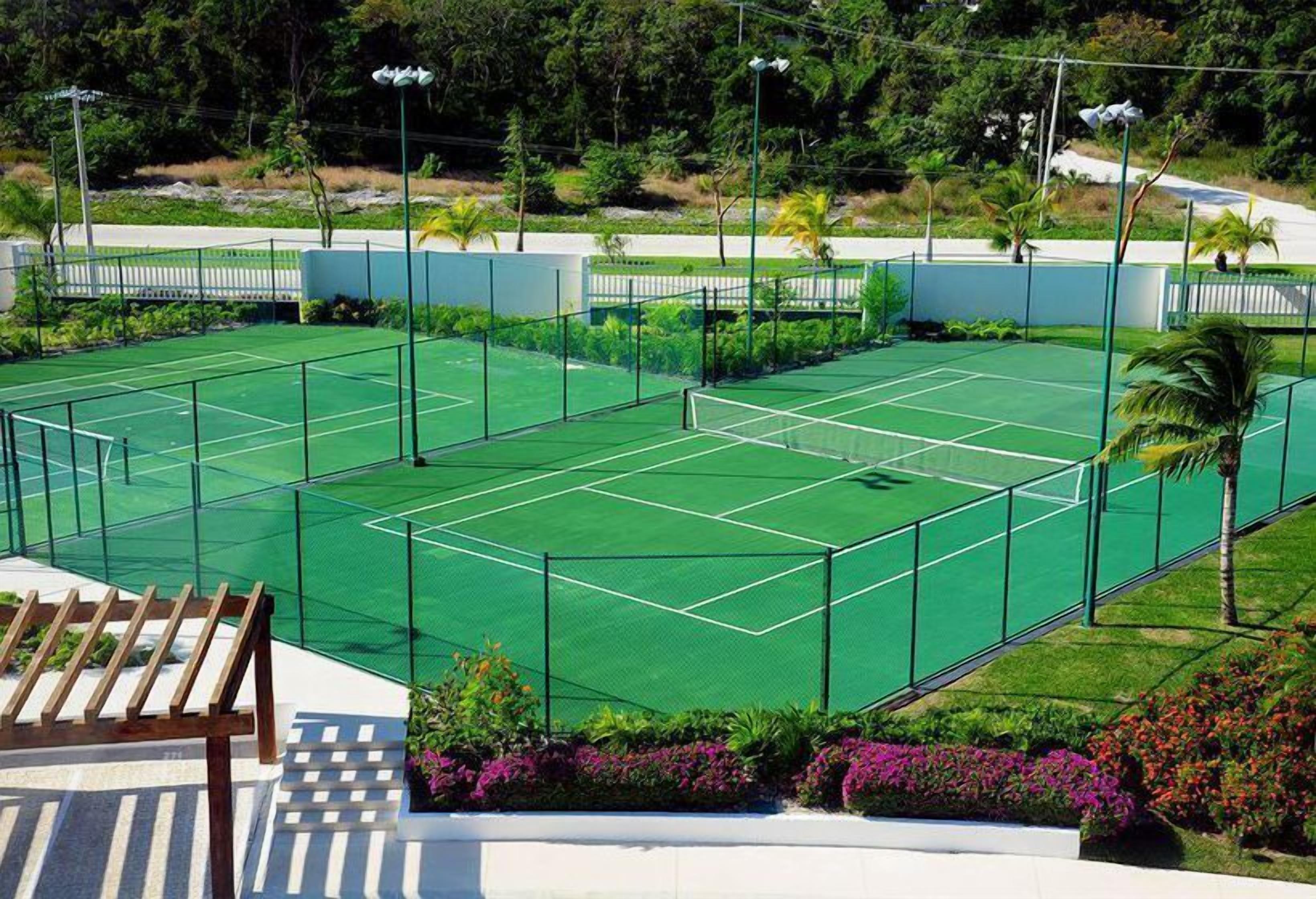 A tennis court with a wooden bench and surrounding greenery.