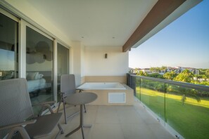 A balcony with a glass balustrade, a seating area with two chairs, a small table, and a built-in bathtub. - MareAzul Apartment 631 by Realty Group (Playa del Carmen)