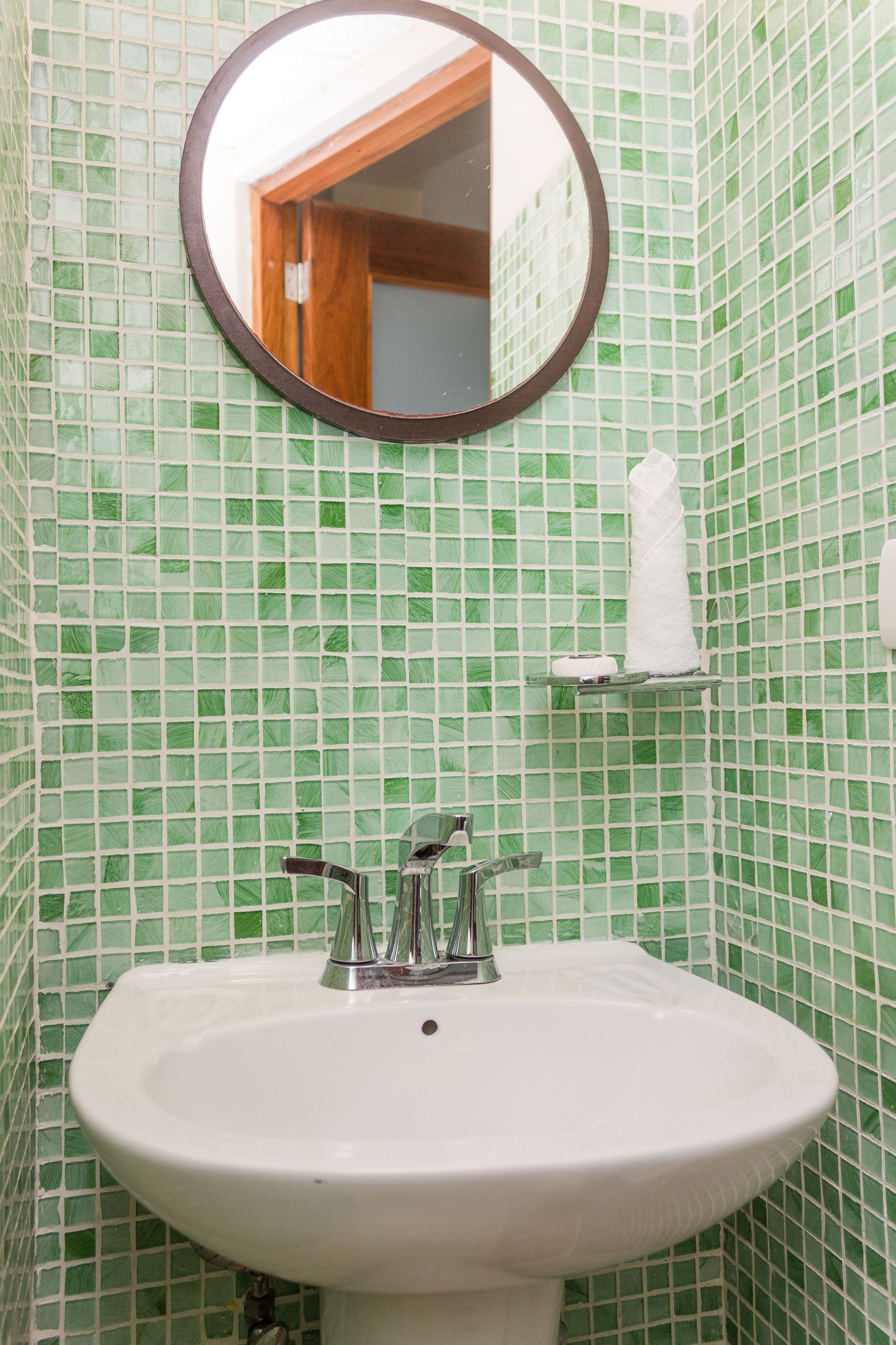 A bathroom with a white sink, a mirror, and green mosaic tiles.
