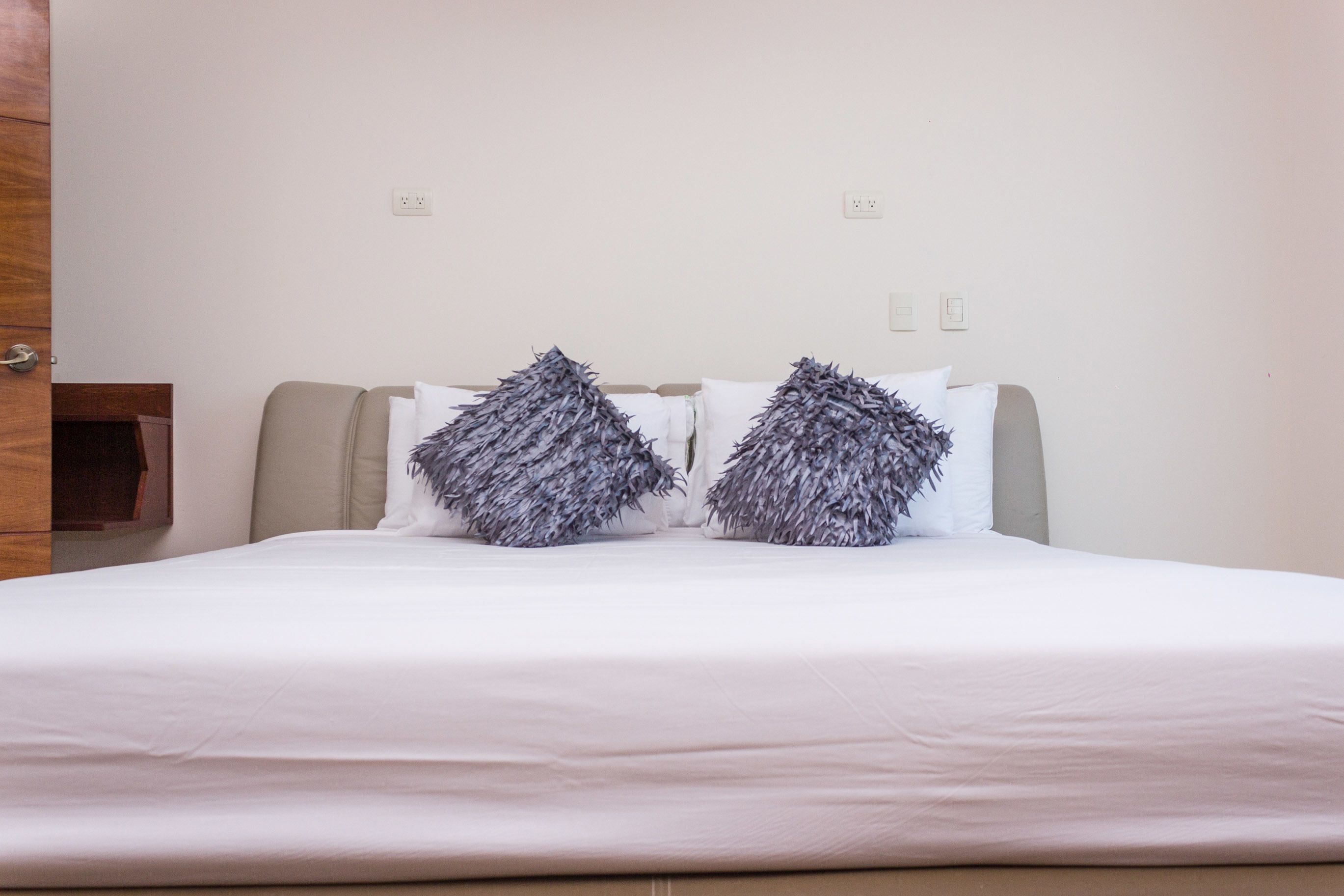 A neatly made bed with white linens and two decorative pillows.
