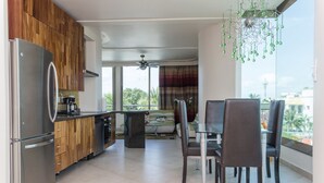 A modern kitchen with wooden cabinets, a stainless steel refrigerator, and a dining area with a glass table and chairs. - Mimosa Penthouse 2 by Realty Group (Playa del Carmen)