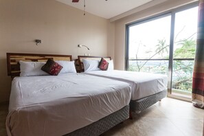 A hotel room with two beds, a large window with a view of palm trees, and a ceiling fan.