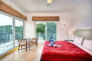 A bedroom with a large bed, a desk, and chairs. There is a window with a view of trees. - Via 38 PH Fuego by Realty Group (Playa del Carmen)