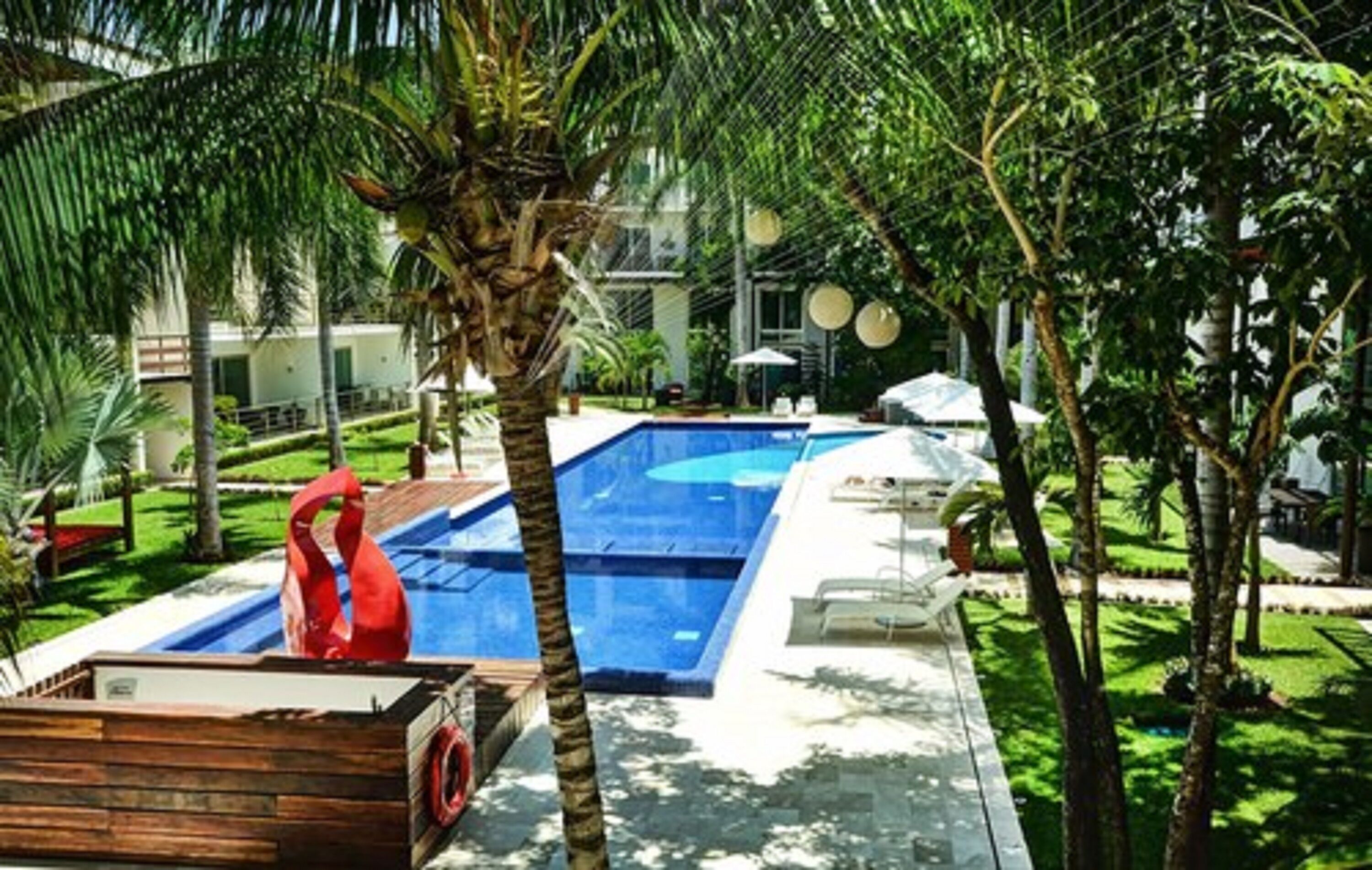 A pool area with a wooden deck, palm trees, and lounge chairs.