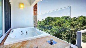 Un baño moderno con una bañera grande, cabina de ducha con mampara de vidrio y vistas a un bosque verde y frondoso.
