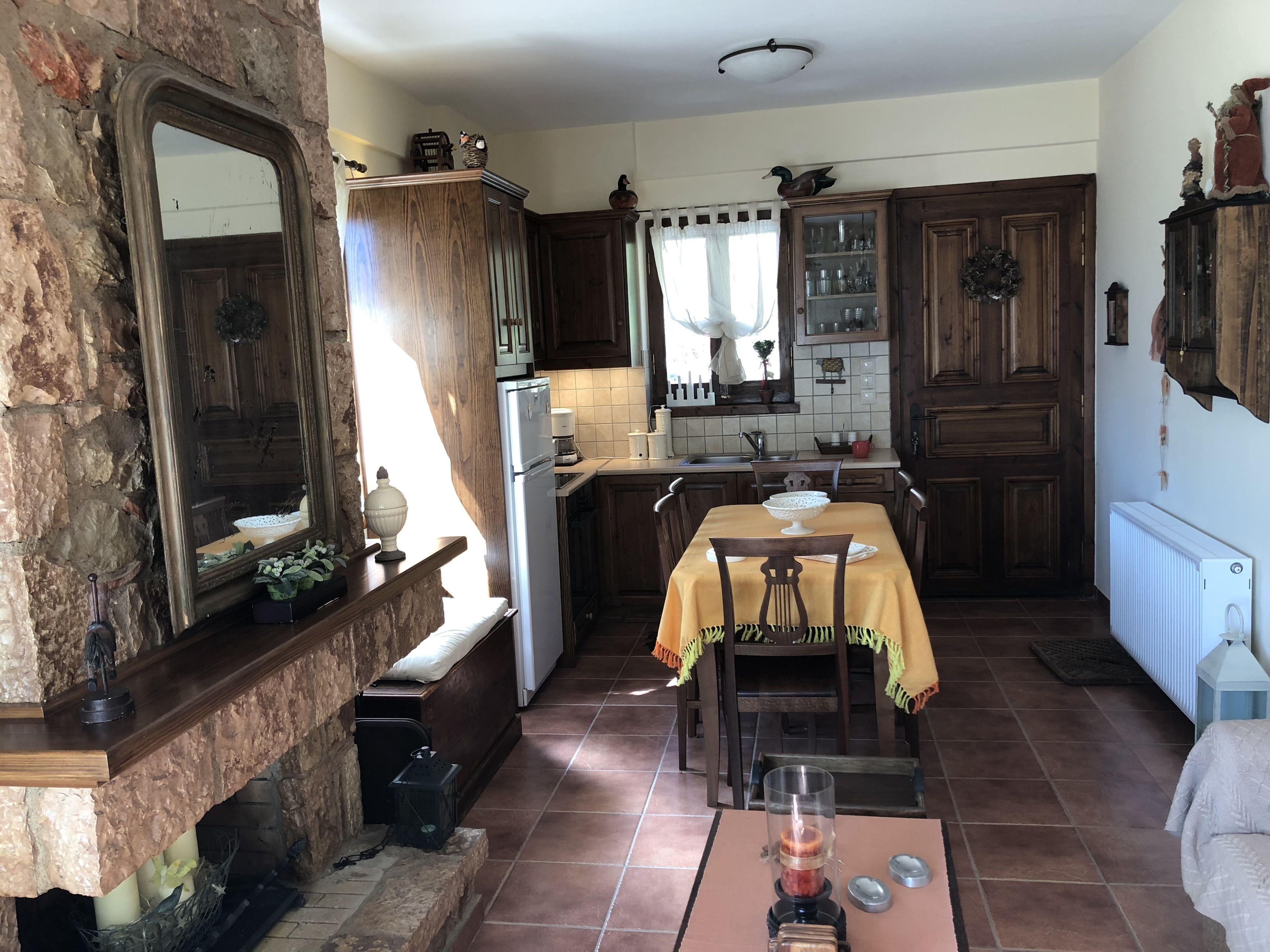 Une cuisine rustique avec des meubles en bois, une cheminée en pierre et une table à manger dressée pour deux personnes.