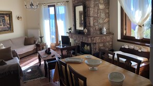 A cozy living room with a stone fireplace, a dining table with chairs, a sofa, and a chandelier. - Arahova Cozy Apartment (Distomo-Arachova-Antikyra)