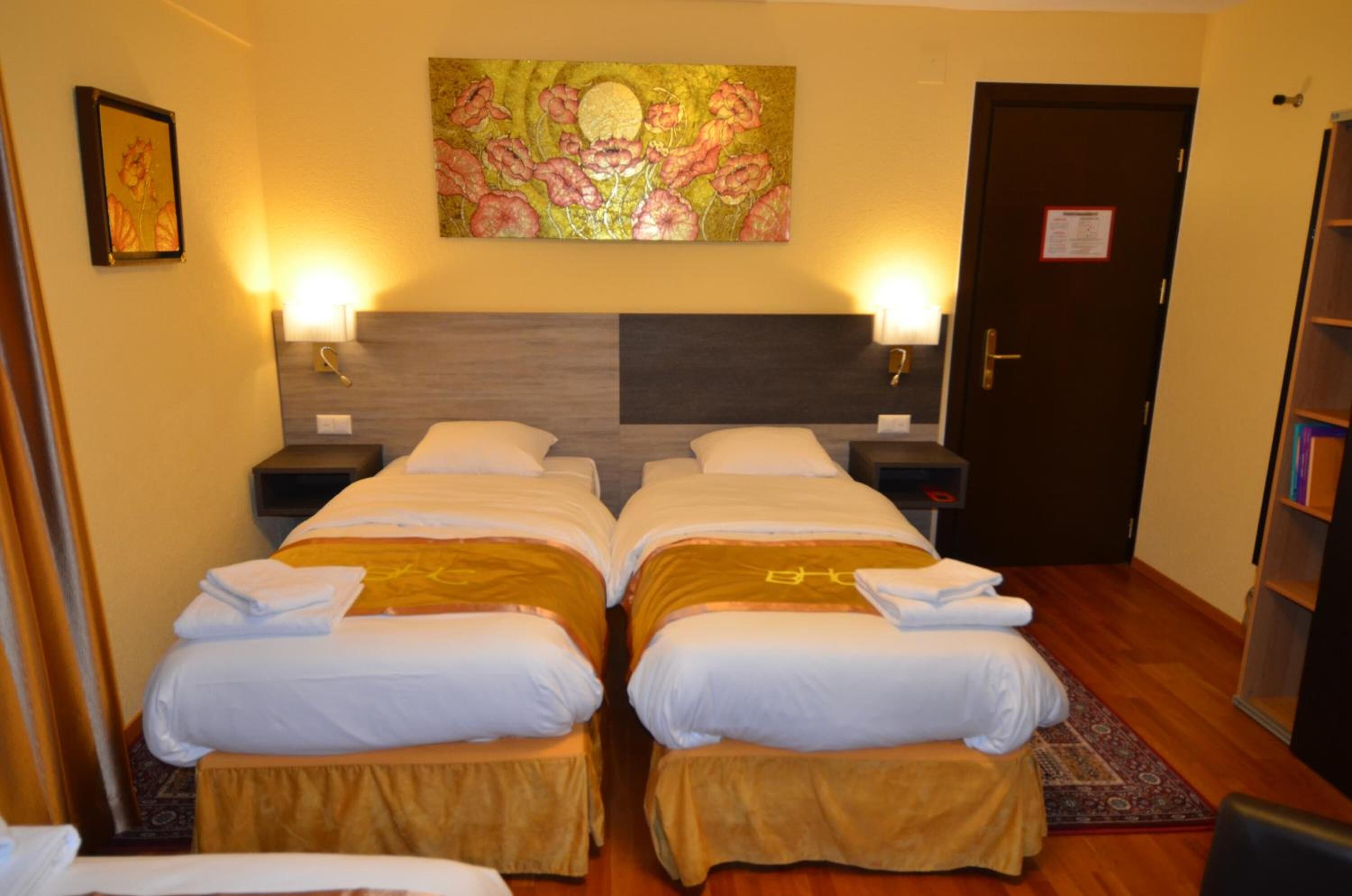 Habitación de hotel con dos camas individuales, un cuadro grande en la pared y una puerta con un letrero.