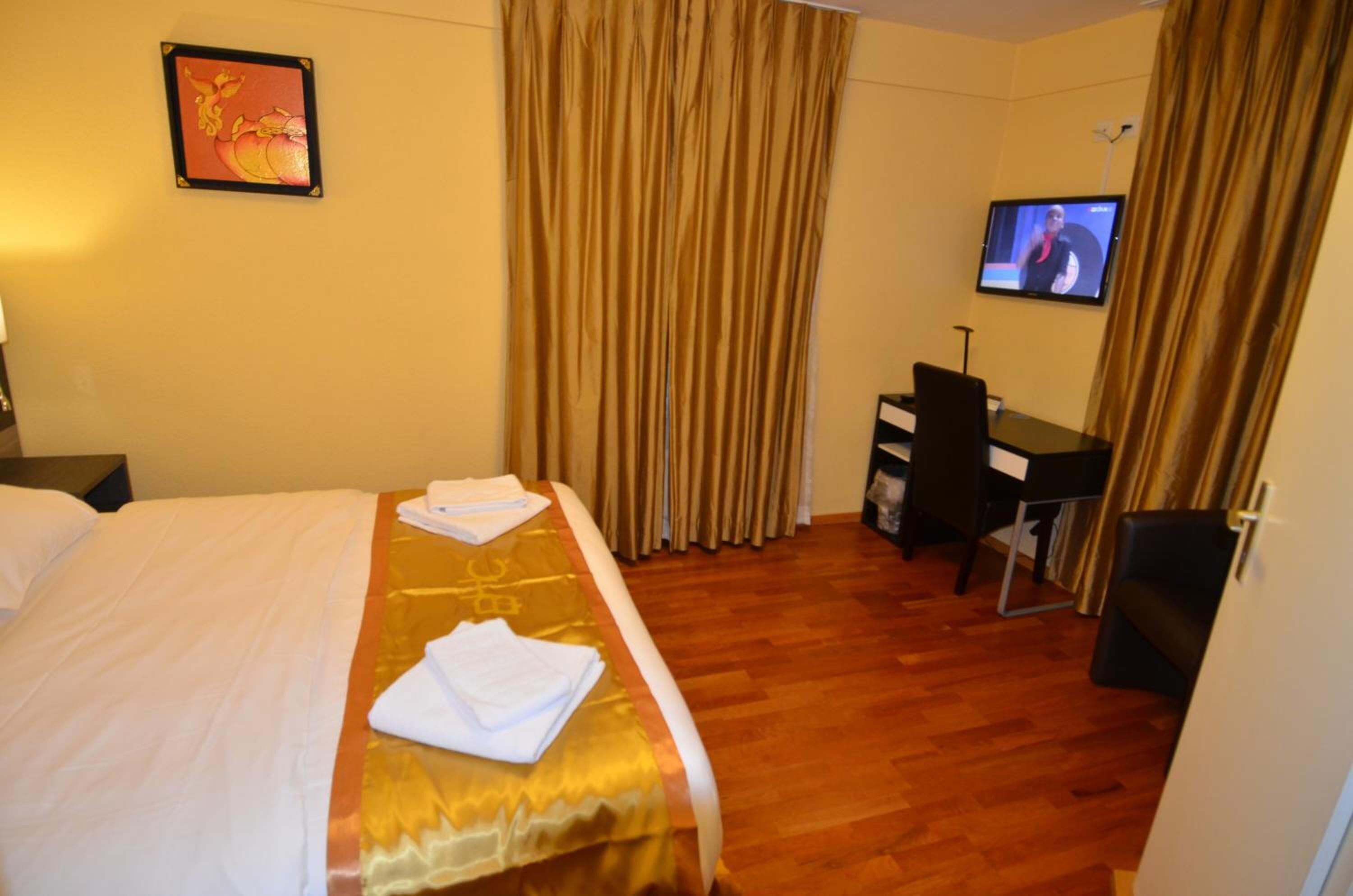 Ein Hotelzimmer mit Bett, Schreibtisch, Fernseher und Vorhängen.