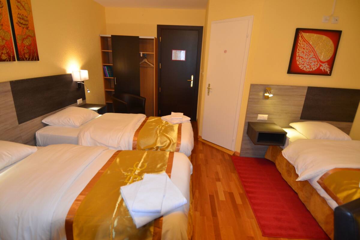 A hotel room with three single beds, a wooden floor, a red rug, and a wardrobe.