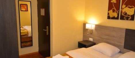 A hotel room with a bed, a nightstand, a mirror, and artwork on the wall.