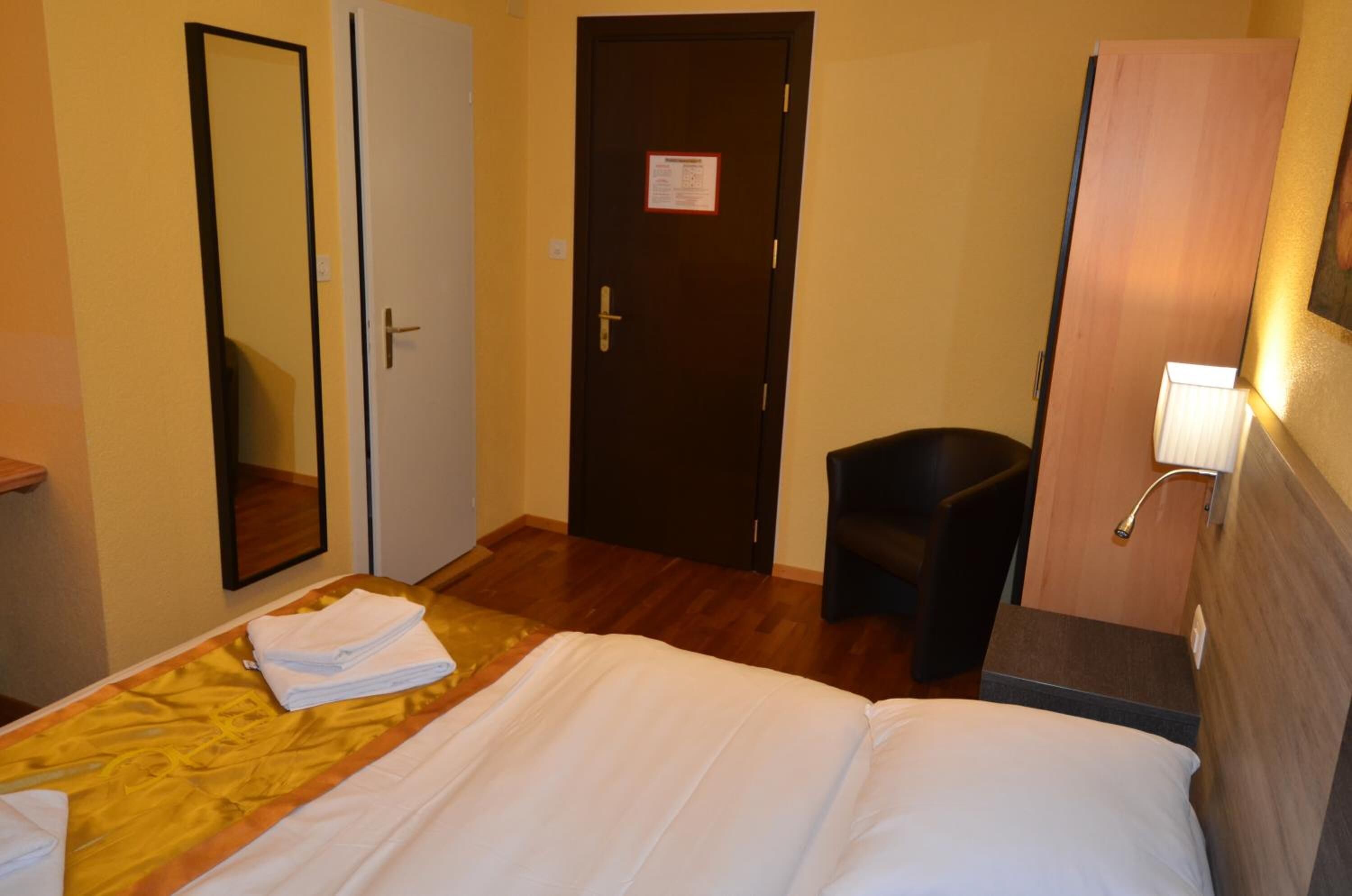 A hotel room with a bed, a desk, a chair, a mirror, and a door.
