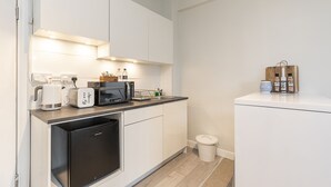 Une cuisine compacte avec des meubles blancs, un réfrigérateur noir, une machine à café, un grille-pain et un four à micro-ondes.