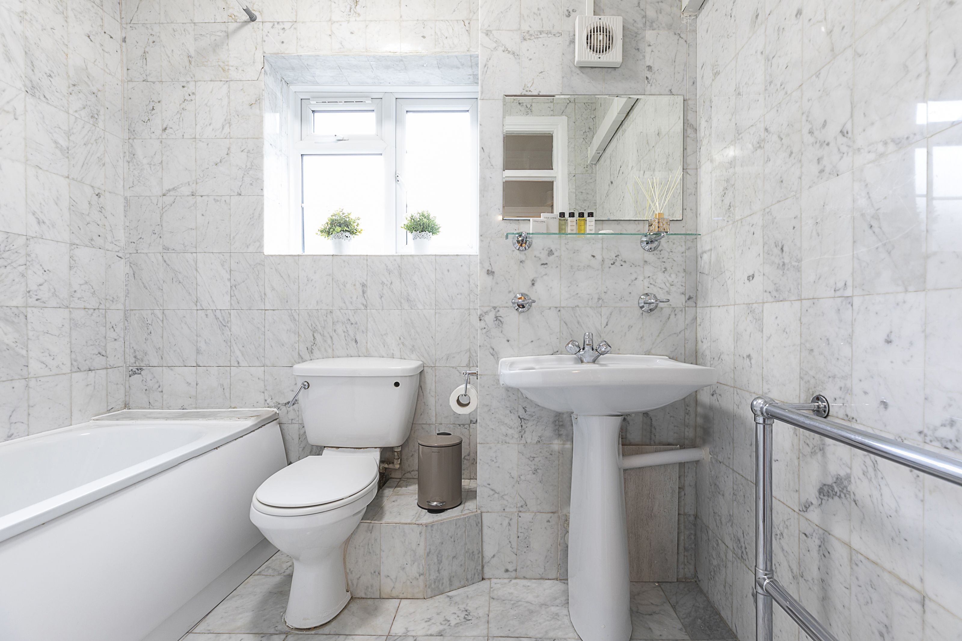 Een moderne badkamer met een badkuip, toilet, wastafel en een raam met planten.