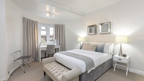 Une chambre bien rangée, avec un lit, des tables de chevet, un bureau et une fenêtre avec des rideaux.