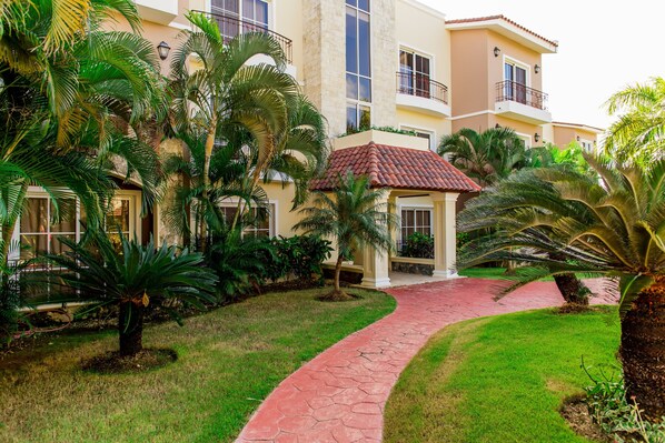 A hotel with a red-tiled roof, a paved walkway, and lush greenery including palm trees.