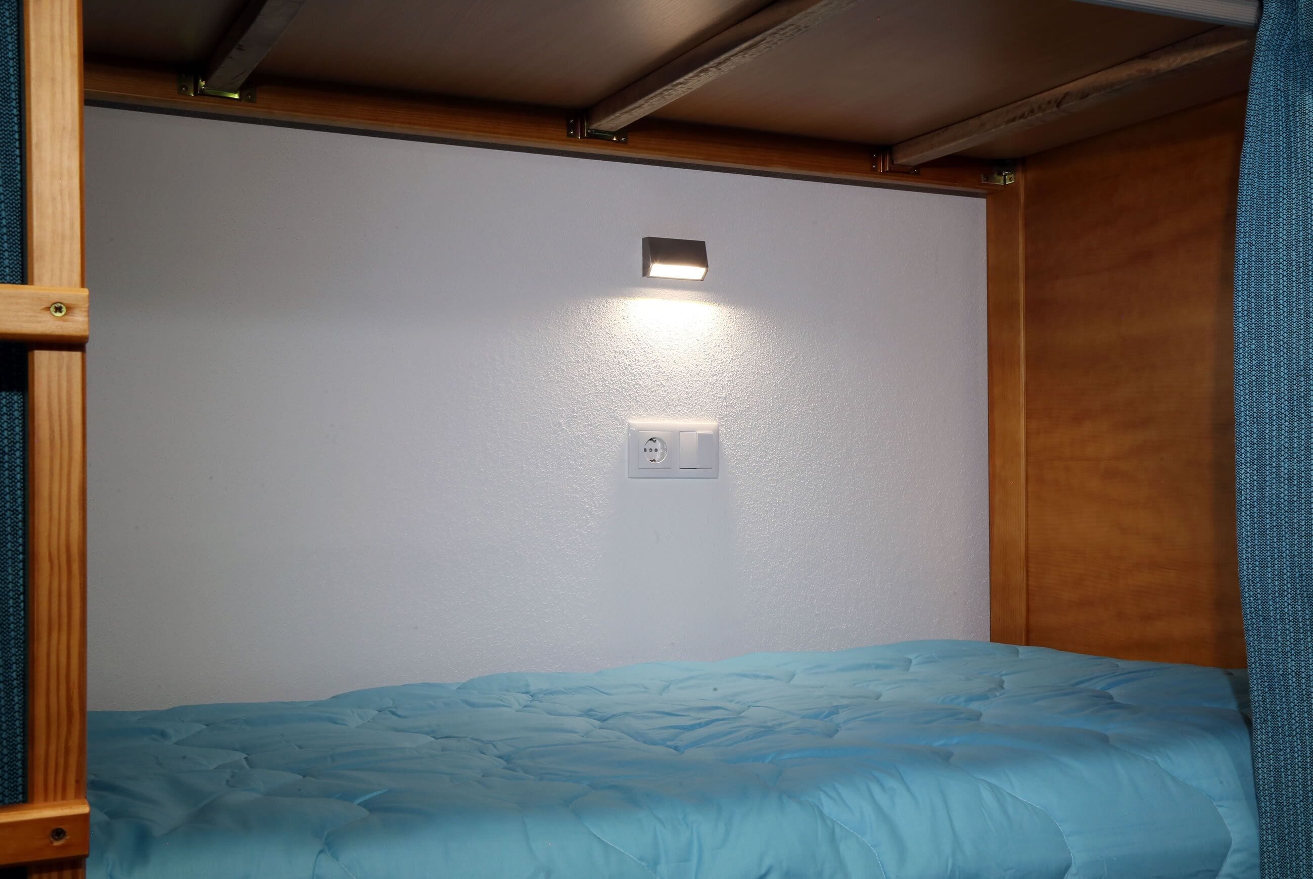 Habitación pequeña con una cama individual, una lámpara en la pared y un enchufe.